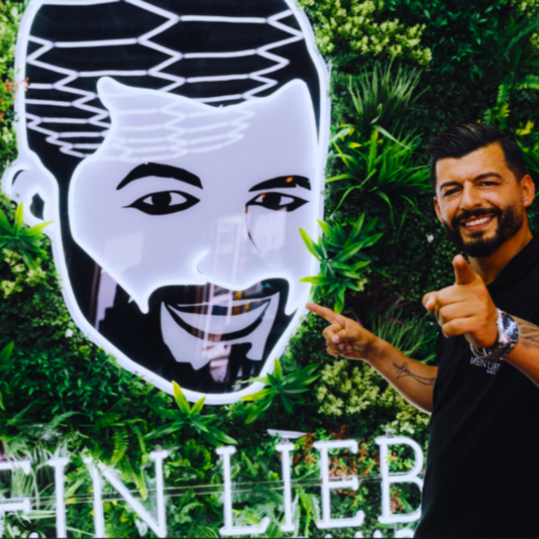 LED Leuchtschild mit personalisiertem Porträtlogo vor grüner Pflanzenwand – individuelles Leuchtschild logo für Firmenkunden